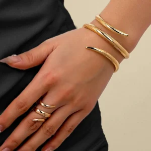 Sculptural polished gold open bangle with matching ring on hand against black fabric